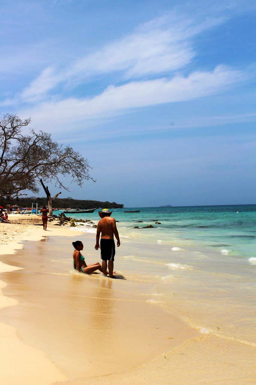 A couple relaxing by the turquoise ocean on a sunny tropical beach, with clear blue skies, gentle waves, and golden sand — a peaceful romantic travel moment captured by the sea.